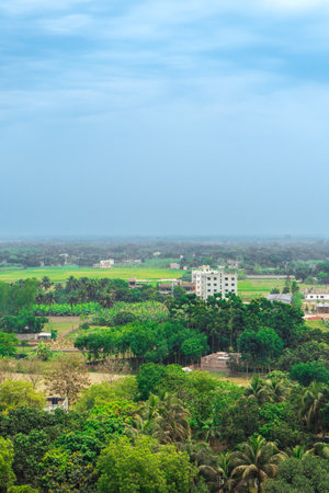 serene rural aerial view landscape with green fields, scattered buildings, and dense foliage under hazy sky. Bangladesh, Rajshahiの写真素材