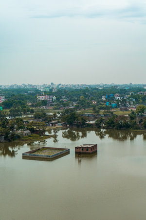 Aerial view of green cityscape with large lake, buildings surrounded by trees under cloudy skyの写真素材