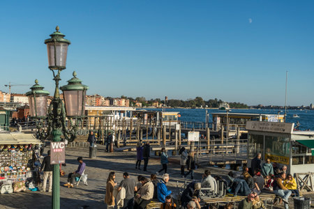 Venice, Italy - 10.11.2024: Lively waterfront scene in Venice, showing people relaxing walking along promenade near San Zaccaria water taxi stationのeditorial素材