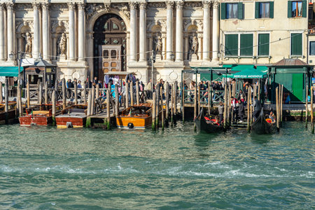 Venice, Italy - 10.11.2024: Gondolas docked along Venetian waterfront with historic building and crowdのeditorial素材