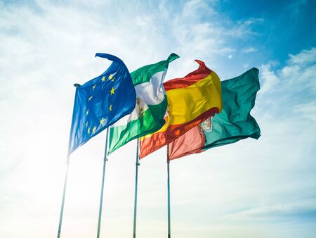 30/09-19, Granada, Spain. Four flags representing EU, Andalusia, Spain and Granada waving in the wind. Backlit by the sun. Taken on the top of torre de la vela of Alcazaba.の写真素材