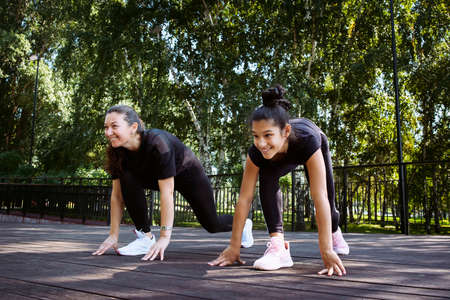 mom and daughter in sportswear on a sunny summer day on the embankment in the park doing fitnessの写真素材