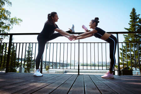 mom and daughter in sportswear on a sunny summer day on the embankment in the park doing fitnessの写真素材