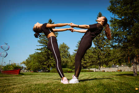 mom and daughter in sportswear on a sunny summer day on the embankment in the park doing fitnessの写真素材