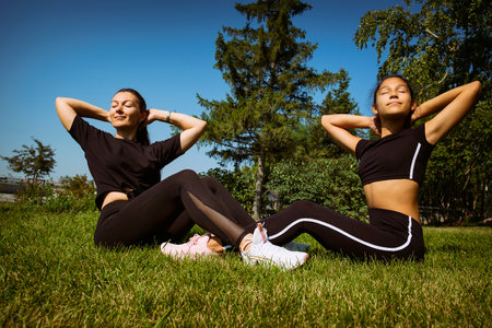 mom and daughter in sportswear on a sunny summer day on the embankment in the park doing fitnessの写真素材