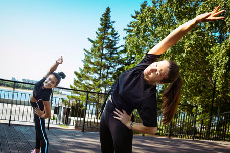 mom and daughter in sportswear on a sunny summer day on the embankment in the park doing fitnessの写真素材