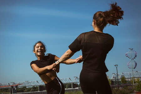 mom and daughter in sportswear on a sunny summer day on the embankment in the park doing fitnessの写真素材