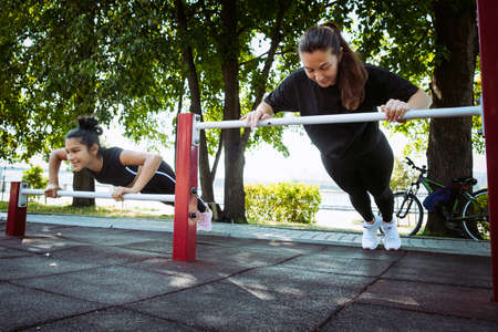 mom and daughter in sportswear on a sunny summer day on the embankment in the park doing fitnessの写真素材