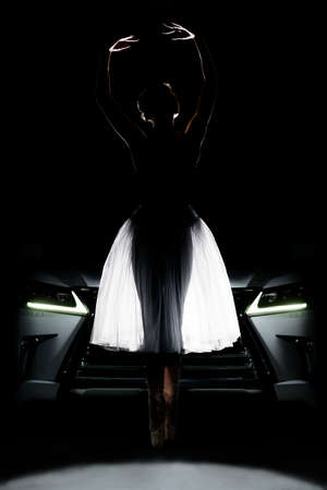 an emotional ballerina in a translucent skirt poses against the silhouette of a carの写真素材