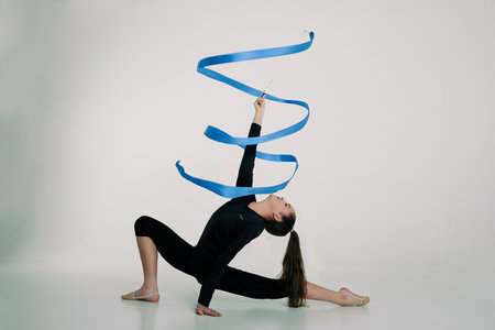 a girl from rhythmic gymnastics in a bodysuit rotates a ribbon sitting on a half-step