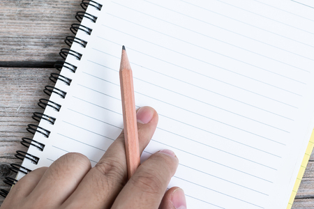 Hand Hold Pencil with Notebook on wood backgroundの写真素材