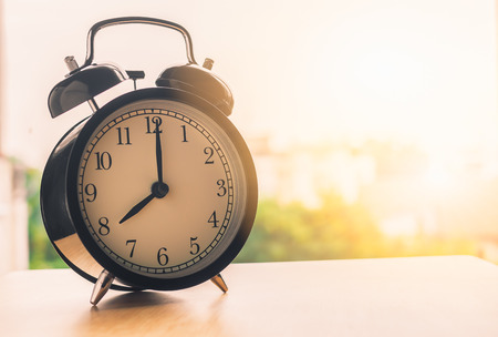 Vintage alarm clock on wood table beside window at morning time  alarm clock show 8 oclockの写真素材