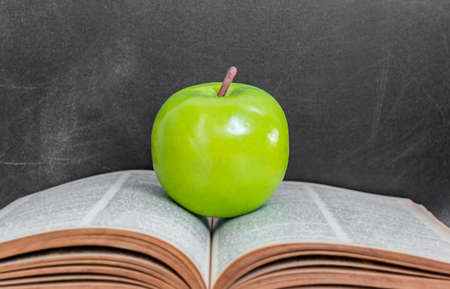 Green apple on old  open book over black chalkboard backgroundの写真素材