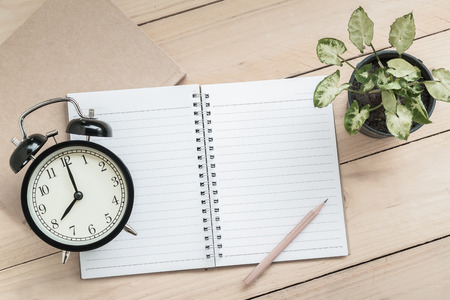 Notebook, pencil, retro clock and plant on wood table backgroundの写真素材
