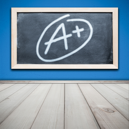 Grade a plus on black chalkboard with cement wall painted blue color and wood floor texture backgroundの写真素材