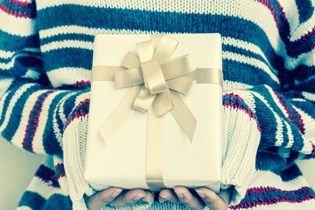 Women hand hold a white gift box with gold ribbon in vintage toneの写真素材