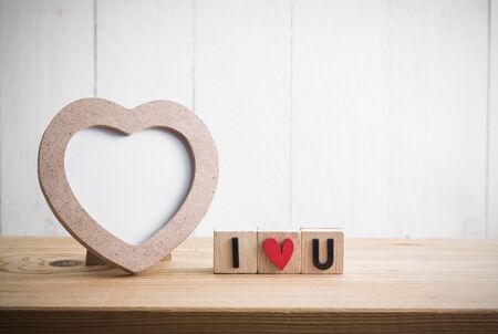 Heart shaped photo frame with "i love u" in cube on wood tableの写真素材