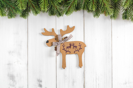 Christmas fir tree branches with reindeers ornament on white rustic wooden background with copy space for textの写真素材