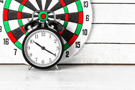 Dartboard with Alarm Clock on white wood.