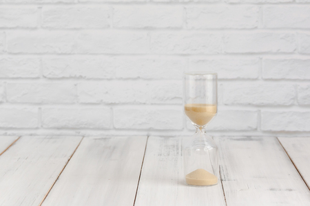 Hourglass on white wood table over white brick background with copy space.の写真素材