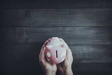 Hands protect piggy bank on wood table background.  Saving safety concept.