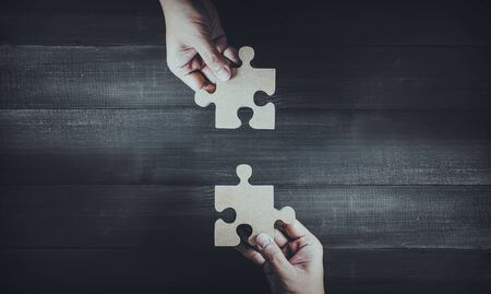 Two hands holding wooden jigsaw puzzle pieces and solving put pieces of the puzzle together. Business solving , Teamwork and partnership conceptの写真素材