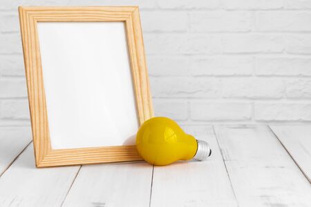 Photo frame and yellow light bulb on white wood table with copy sapce, idea concept.の写真素材