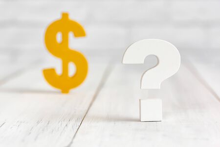 Question mark with dollar sign on white wood table over white brick background with copy space.の写真素材