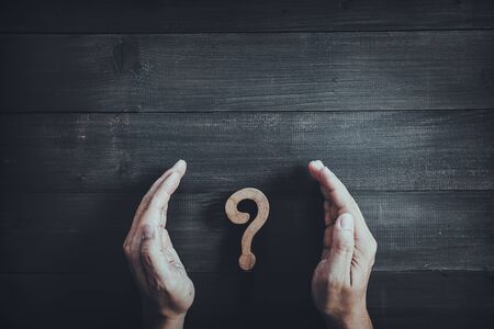 Hands protect wooden question mark on wood table background.  Problem solving concept.の写真素材