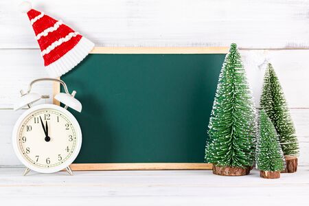 Pine tree with empty black board and alarm clock , christmas hat on white wood background.の写真素材