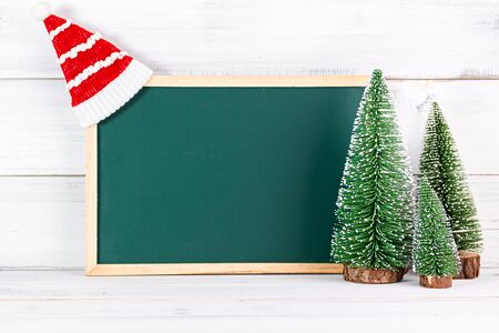 Pine tree with empty black board and christmas hat on white wood background.の写真素材