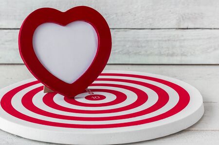 Red Heart Frame on Red dartboard over white wood backgroundの写真素材