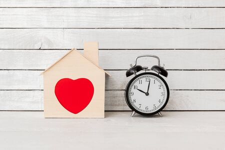 Wood Home Shaped with red heart and alarm clock on white wood over white wood background.