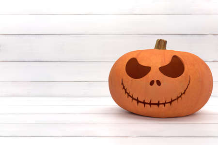 One spooky halloween pumpkin, Jack O Lantern, with an evil face and eyes on a white wood background.の写真素材