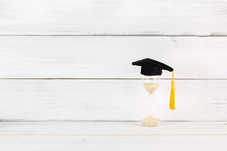 Education Hat with hourglass on white wood background.の写真素材