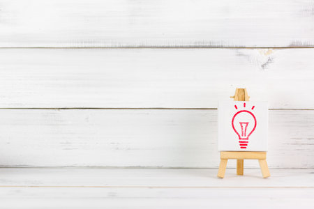 Red Light Bulb Icon on Wooden Easel: Concept of Innovation and Bright Ideasの写真素材