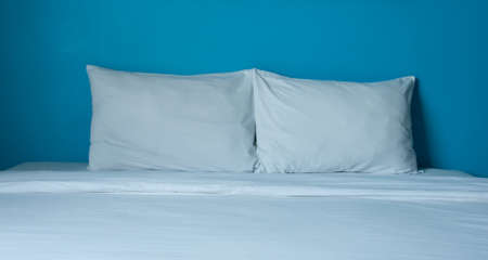 The couple white pillow on white bed in bright blue roomの写真素材
