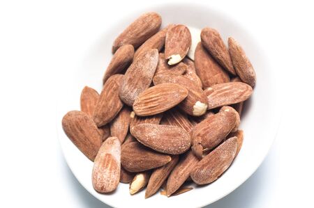 White dish of salted and toasted almonds on a white backgroundの写真素材