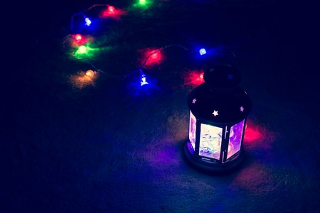Holiday Greeting Card or Background. Christmas Lights and Candle Lantern on Dark Background....