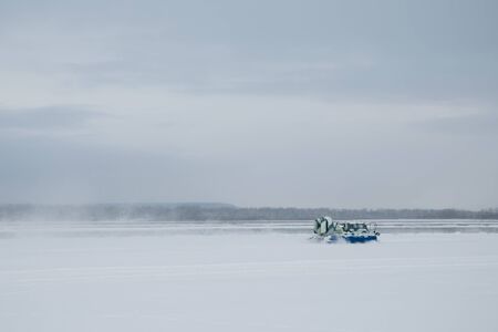 A blue hovercraft rushes along the snowy Volga River. A snow blizzard rises about her. High quality...
