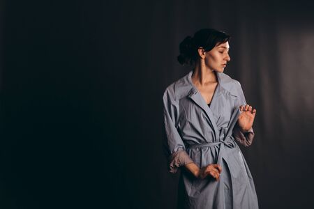 Girl with ponytail hair tightens the belt of a blue trench coat. Studio shot with empty space. Girl with ponytail hair tightens the belt of a blue trench coat. Studio shot with empty space.の写真素材