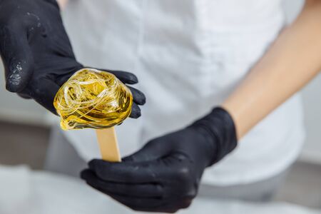 The wax is wound on a wooden spatula. The wax is intended for depilation. The spatula is held by...