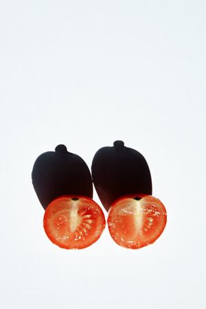 Unusual associations. Two ripe cherry tomato halves lie in sun. The section shows tomato seeds. Vegetables cast a shadow of an unusual shape in the form of a breast. Tomato juice glistens in the sun.の写真素材