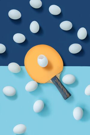 The yellow racket is in the middle of the table. There is a split egg on the racket. There are other eggs lying around. The frame is divided in blue into two parts. Flat layの写真素材