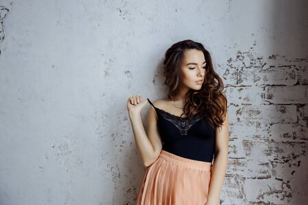 A beautiful girl stands against the wall and looks away. The girls hand adjusts the strap on the...