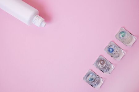 Four types of colored lenses in blisters lie at the edge of the frame. There are different colors: brown, blue, green. In the other corner is a solution for lenses. Items are found on pink background.の写真素材