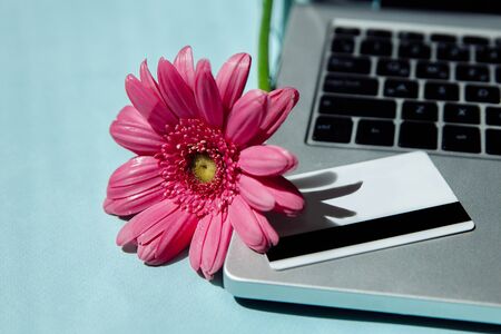 On the silver laptop is a white Bank card. Next to it is a pink Astara. These items are on the blue table. Illustration of online purchases.の写真素材