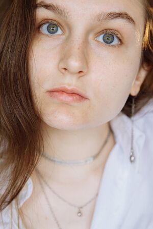 A brunette girl with natural features looks piercingly at the viewer. Shes wearing a white shirt and silver jewelry High quality photoの写真素材