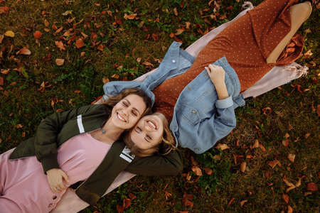 Young women lie on the autumn grass. Dry yellow leaves lie around. Women smile sincerely. High quality photoの写真素材