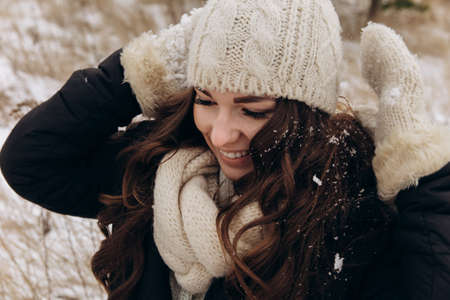 Portrait of a Russian woman in a white hat and gloves. she pops the hat. There is snow in the womans...